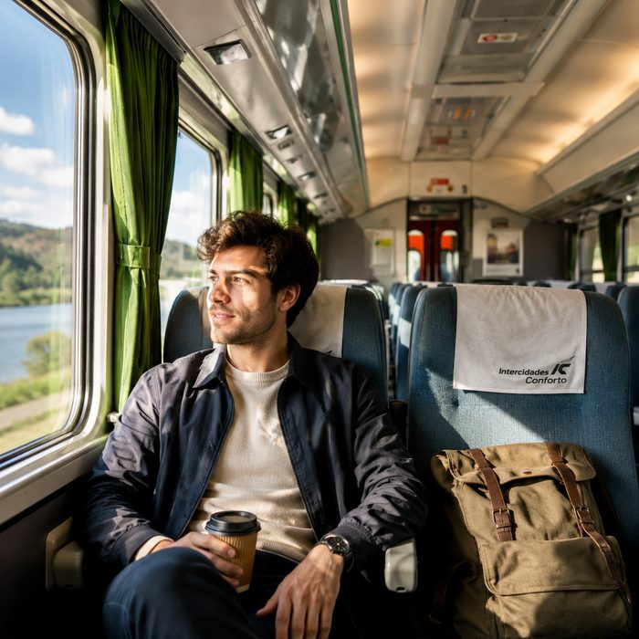 Passenger relaxing in an Intercidades Conforto first-class seat with a coffee, next to green curtains and a window view of the Douro